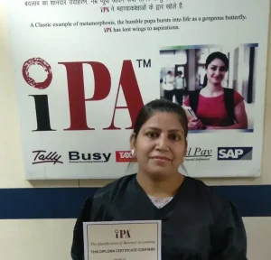 Student holding her IPA diploma certificate in front of the IPA software poster at E-54, Laxmi Nagar