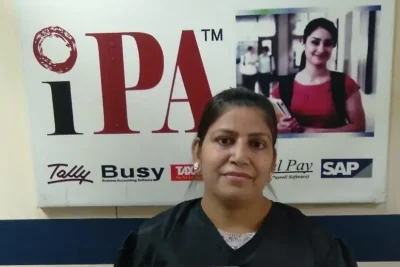 Student holding her IPA diploma certificate in front of the IPA software poster at E-54, Laxmi Nagar